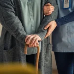 Nurse assisting older patient with walking stick