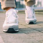 Female feet in white sneakers walking on the sidewalk low angle retro colors.