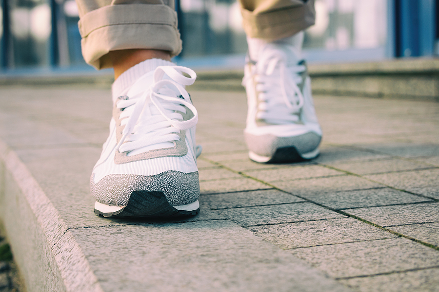 Female feet in white sneakers walking on the sidewalk low angle retro colors.